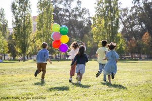 spielende Kinder auf einer Wiese mit Luftballlons